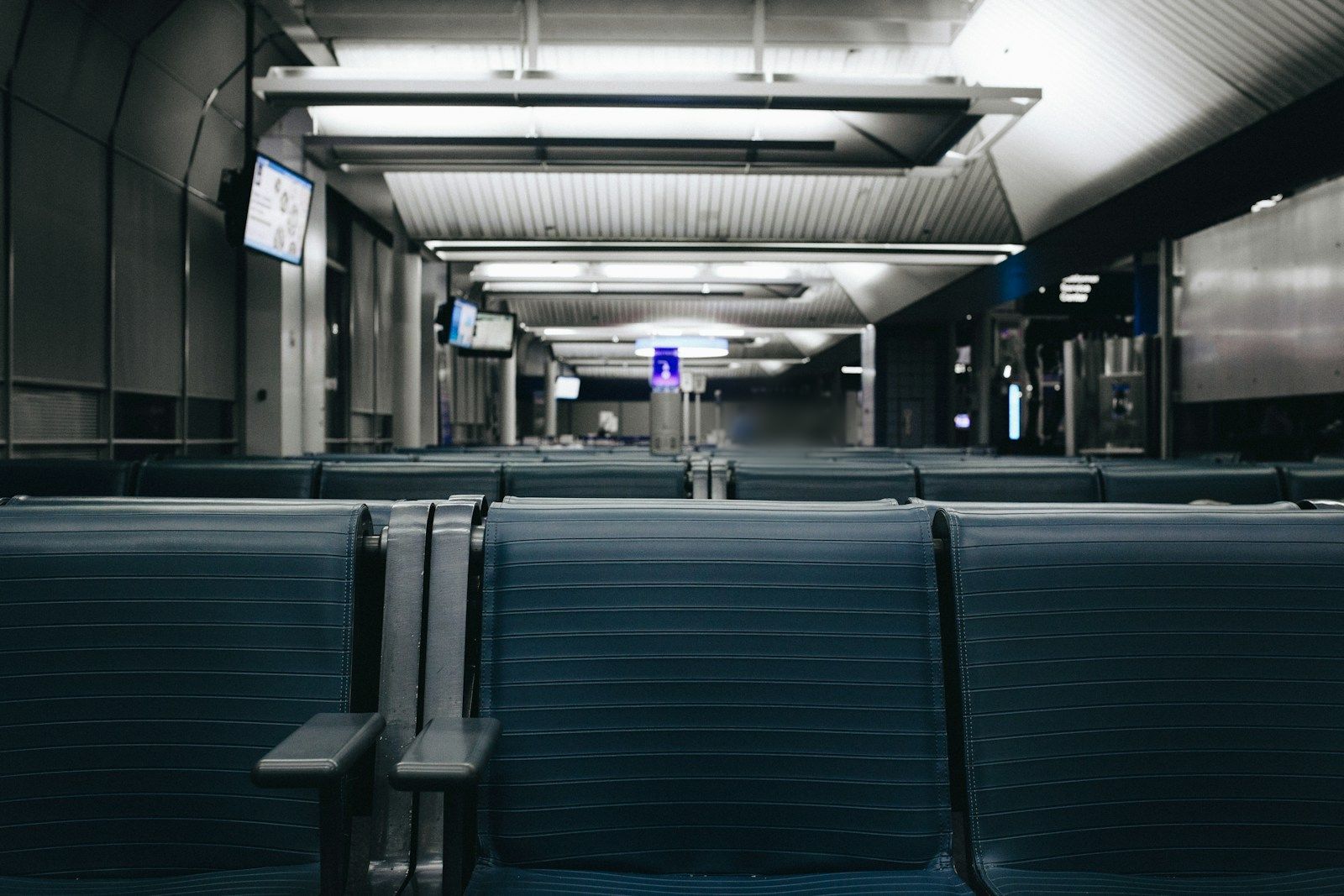 Rows of empty blue seats in a dimly lit airport gate area.